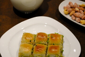 Traditional Turkish pistachio mini square baklava close-up. Pistachio baklava. Turkish syrup desserts. Ramadan, iftar menu. Sliced mini baklavas on a white plate. Turkish desserts.
