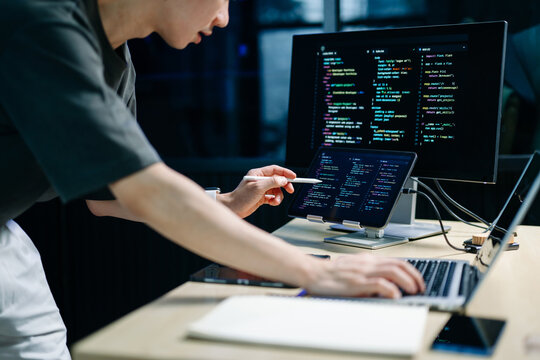 Programmer using stylus and laptop to write code at night. Coding workspace with tablet, monitor, and dark theme