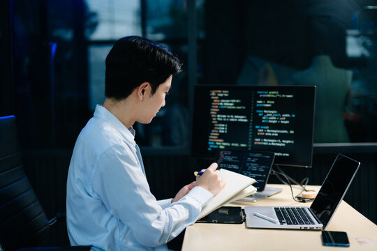 Young male programmer working with tablet and screen displaying code. Modern tech office setup, great for software