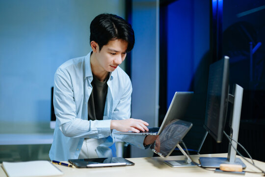 Young male programmer working with tablet and screen displaying code. Modern tech office setup, great for software