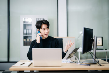 Asian man using laptop and tablet while sitting at her working place. Concentrated at work.