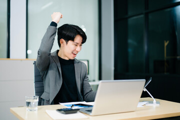 Asian businessman celebrating victory at desk with a phone. Captures success, motivation,...