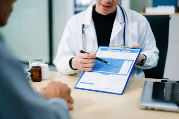 Asian doctor points to a medical form while consulting a patient in a bright clinic office. Concept...
