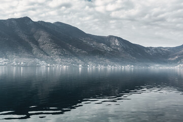Low fog and dramatic reflections over calm water in Kotor Bay surrounded by mountains, Montenegro