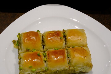 Traditional Turkish pistachio mini square baklava close-up. Pistachio baklava. Turkish syrup desserts. Ramadan, iftar menu. Sliced mini baklavas on a white plate. Turkish desserts.
