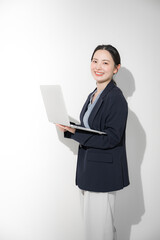 パソコン持って立つスーツを着た若いかわいい女性のビジネスイメージ　カメラ目線
