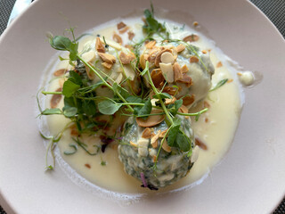 Nettle dumplings on fontina cream, garnished with wild herbs and almond slices