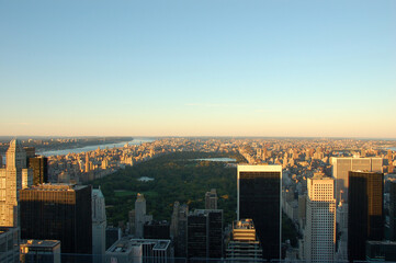 Aerial view of Central Park and Manhattan skyline at sunset in New York City, with tall buildings and soft pastel sky above the urban landscape
