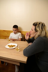 Mother and son drinking tea with pastries at the table in the kitchen.