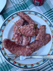 Grilled sausage seasoned with salt, sage leaves lying beside fork on checkered tablecloth, presenting rustic culinary comfort