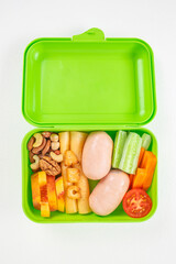 Bright green lunchbox filled with sausages, cheese, nuts, fruits, and fresh vegetables including...