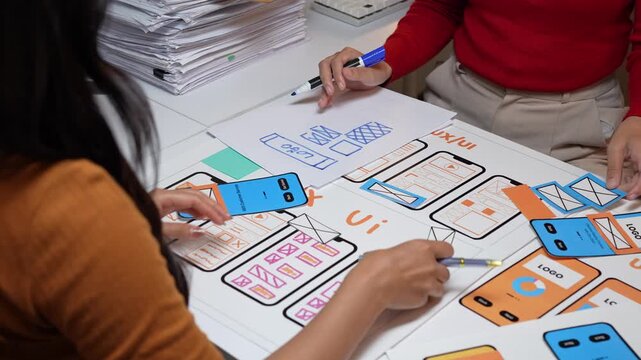 Web designers refining mobile app prototype with paper mockups