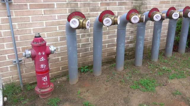 A red fire hydrant stands in front of a row of identical grey pipes