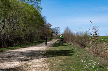 Obraz premium Two cyclists enjoy a sunny ride down a country lane, surrounded by lush greenery.