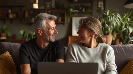 Couple's Digital Moment: A senior couple shares a smile as they sit together, illuminated by the warm glow of a laptop screen. A tender moment of connection. - Powered by Adobe