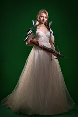 Young pretty blonde with exquisite makeup and hairstyle in a beautiful wedding dress and green...