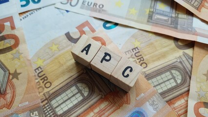 APC acronym made of wooden letter cubes on pile of Euro banknotes. Agenzia per le Politiche del...