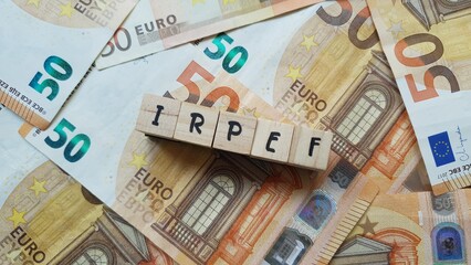 IRPEF acronym made of wooden letter cubes on pile of Euro banknotes. Imposta sul Reddito delle...