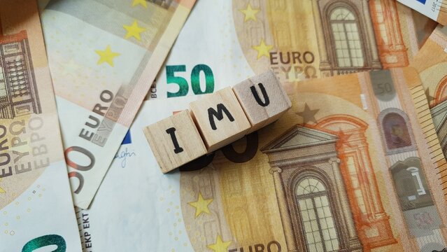 IMU acronym made of wooden letter cubes on pile of Euro banknotes. Imposta Municipale Unica (Unified Municipal Tax, property tax)