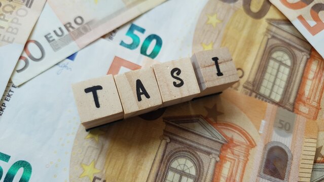 TASI acronym made of wooden letter cubes on pile of Euro banknotes. Tributo per i Servizi Indivisibili (Tax for Indivisible Services)