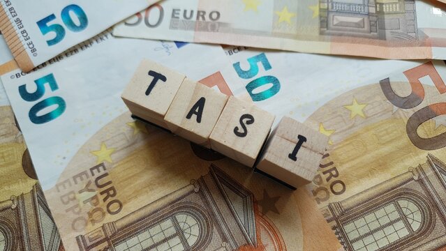 TASI acronym made of wooden letter cubes on pile of Euro banknotes. Tributo per i Servizi Indivisibili (Tax for Indivisible Services)