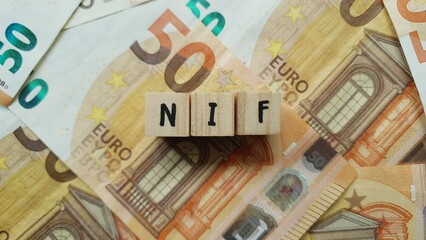 NIF acronym made of wooden letter cubes on pile of Euro banknotes. Numero di Identificazione Fiscale (Tax Identification Number)