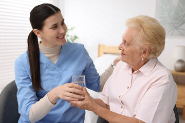 Obraz premium Nurse giving glass of water to senior woman indoors. Home health care service