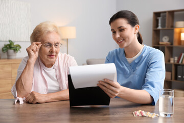 Nurse with clipboard examining senior woman at wooden table indoors. Home health care service