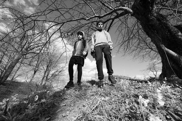 Two young people hiking on a trail, under a large tree. Black and white photography.