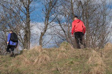 Two young people hike along a path through a winter landscape. Bare trees surround them as they...