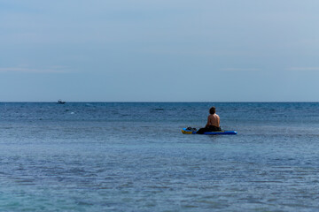 Paddle surfer sitting on his board on calm idyllic blue sea. Perfect moment to take wonderful...