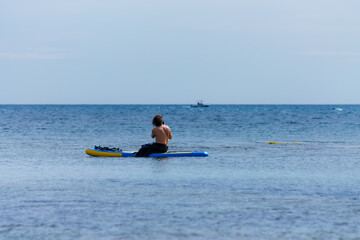 Paddle surfer sitting on his board on calm idyllic blue sea. Perfect moment to take wonderful...