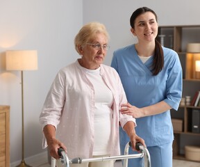 Nurse assisting senior woman with walking frame indoors. Home health care service