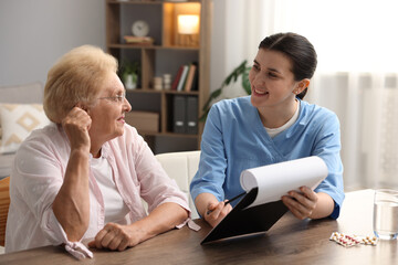 Nurse with clipboard examining senior woman at wooden table indoors. Home health care service