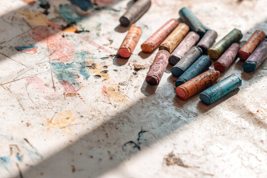 Colorful crayons scattered on white table with broken drawings, sunlight casting shadows, creative and playful atmosphere, art supplies for children and artistic expression