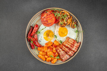 Traditional English breakfast plate with fried eggs, sausages, bacon, baked beans, grilled tomatoes, and mushrooms garnished with fresh herbs on a dark background