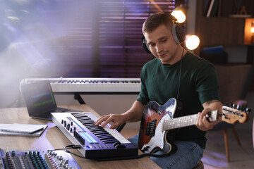 Man in headphones working with MIDI keyboard and guitar at table in home studio
