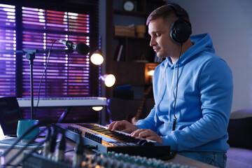 Man in headphones working with MIDI keyboard at table in home studio