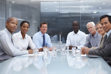 Group of diverse professionals at a conference table in a modern office setting looking at camera .