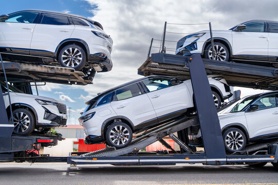 Modern white SUVs stacked on a multi-level car transporter trailer, ready for delivery or export. New white SUVs loaded on car carrier trailer, vehicle logistics and transportation industry concept - Powered by Adobe