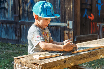 Little boy wearing a cap is focused on shaping clay in the yard of a rustic village house, enjoying a sunny day outdoors