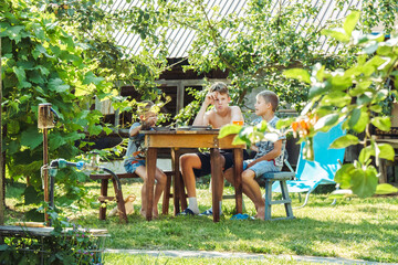 Three brothers are having lunch at a round wooden table in a lush garden, surrounded by greenery and sunlight