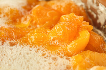 Orange color apricot berries bubbling in a pot during the simmering process for a fresh homemade jam. Shallow depth of field