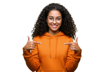 A proud young woman with curly hair and glasses, wearing an orange hoodie, points to herself with a confident smile isolated on transparent background