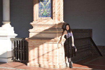 Young, beautiful, brunette woman in a fancy black dress, posing leaning against a brick wall, receiving a play of light and shadow. Concept beauty, fashion, trendy, femininity.