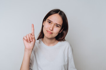 Young woman with a questioning expression holds her finger up in a gesture of thinking during a...
