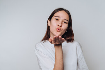 Young woman blows a kiss while posing against a neutral backdrop in a playful moment