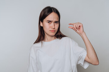 Young woman expressing frustration with a tiny gesture indoors in casual clothing