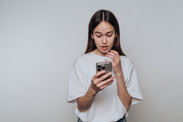 Young woman reacts to surprising message on her smartphone while standing indoors in casual attire