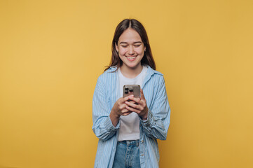 Smiling young woman wearing a striped shirt interacts with her smartphone in front of a bright...